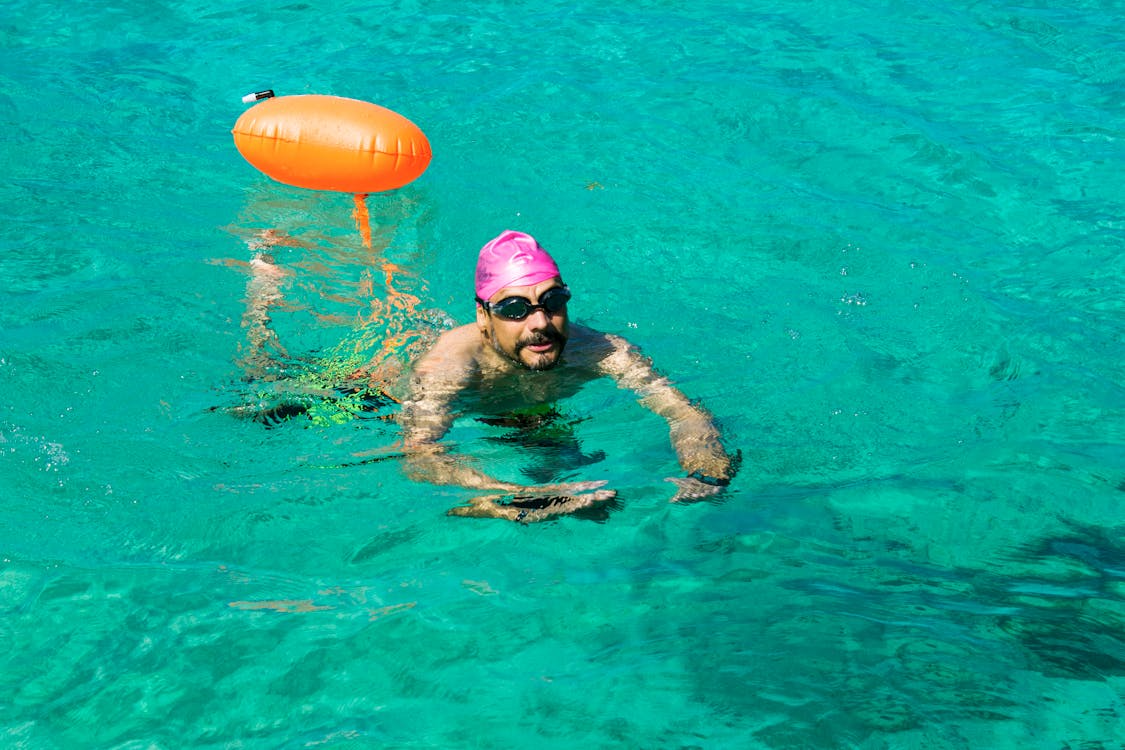 solo swimming safety with a swimmer using a bright swim buoy in clear open water