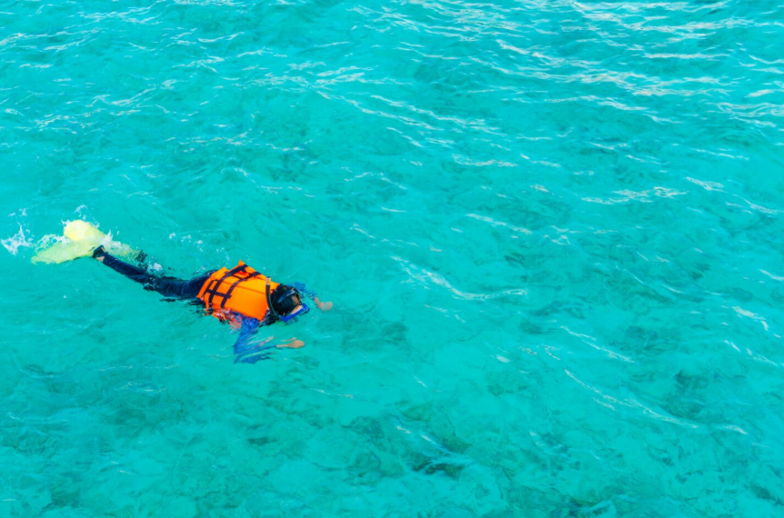 Beginner snorkeling spots with a snorkeler floating in calm turquoise water near shallow reef areas.