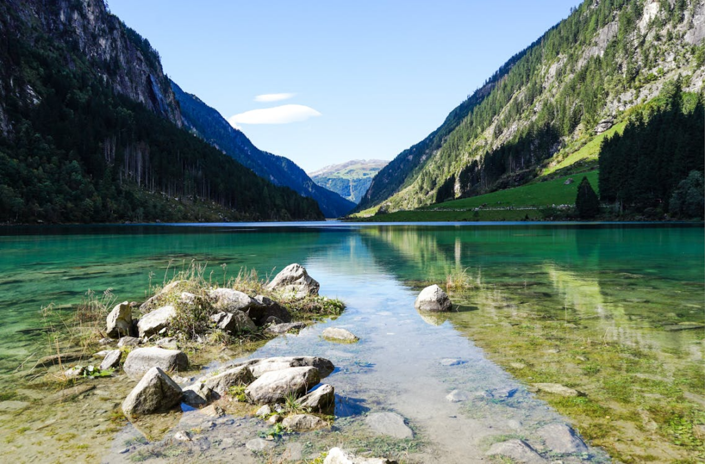 Clearest waters in the world shown in a transparent alpine lake with mountains and visible rocks beneath the surface.
