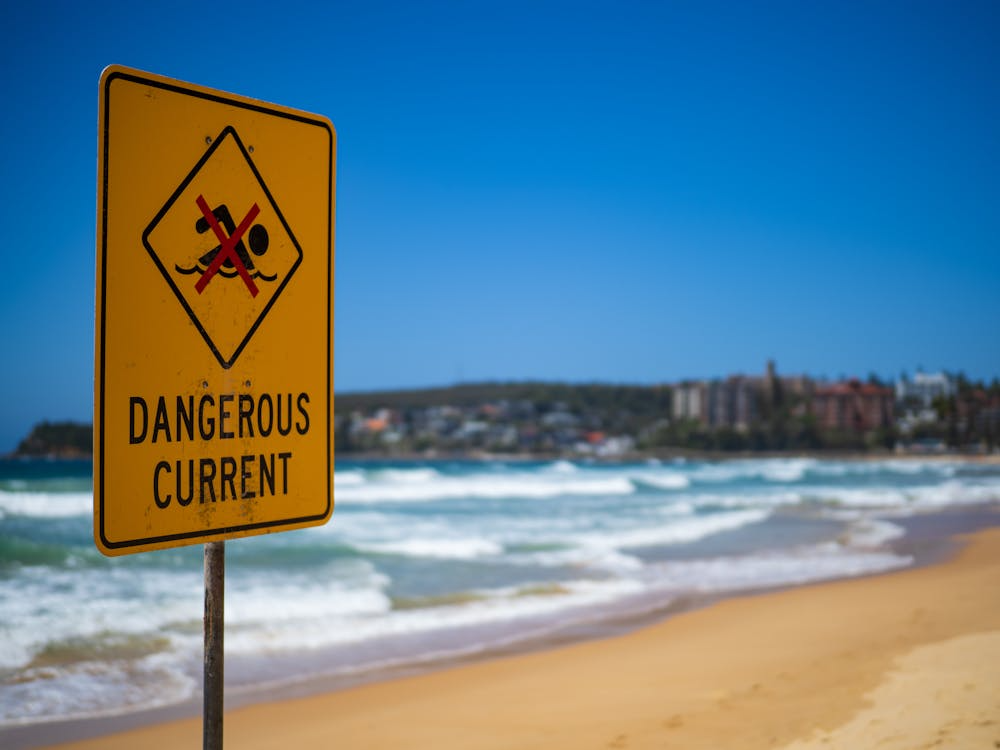 How rip currents form shown by a dangerous current warning sign near rough beach waves.