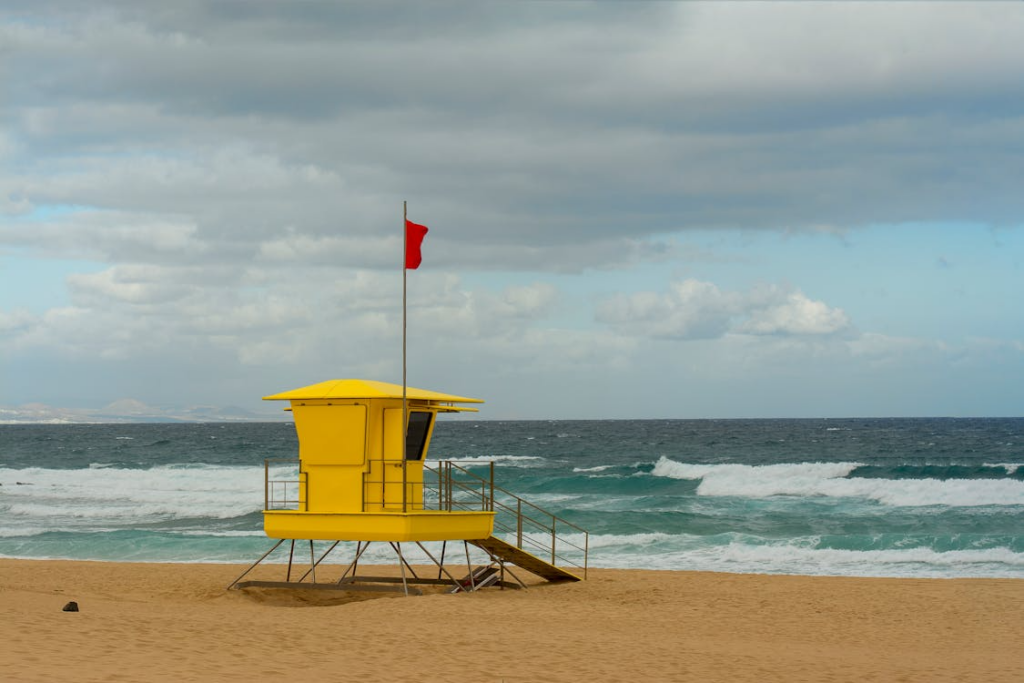 beach safety tips with a red warning flag, lifeguard tower, and rough ocean waves