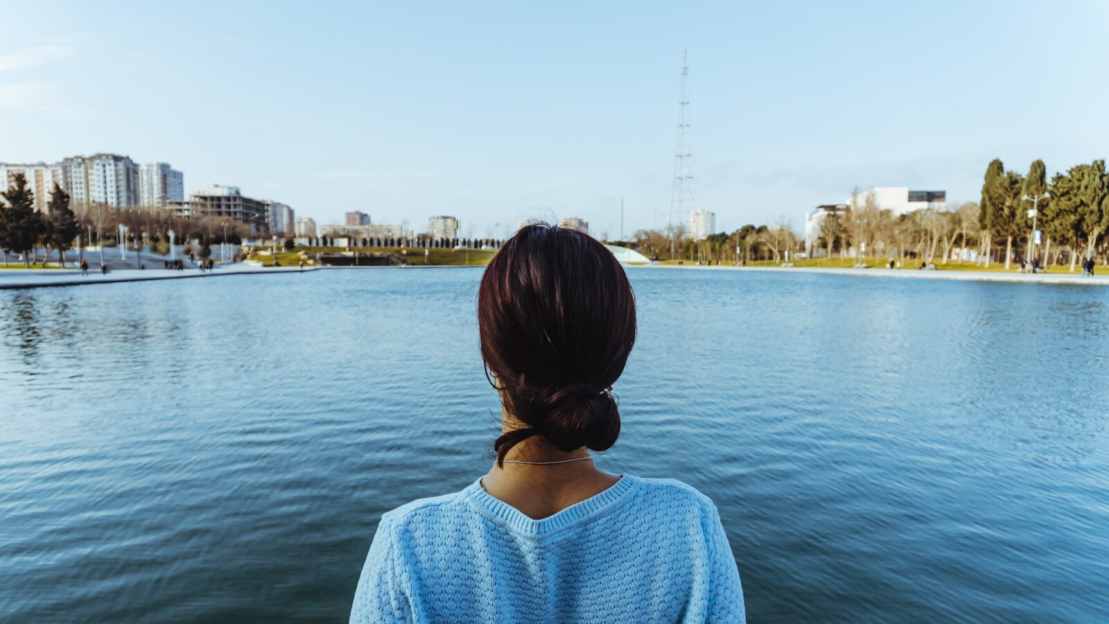 woman in blue knit shirt standing near body of water during daytime